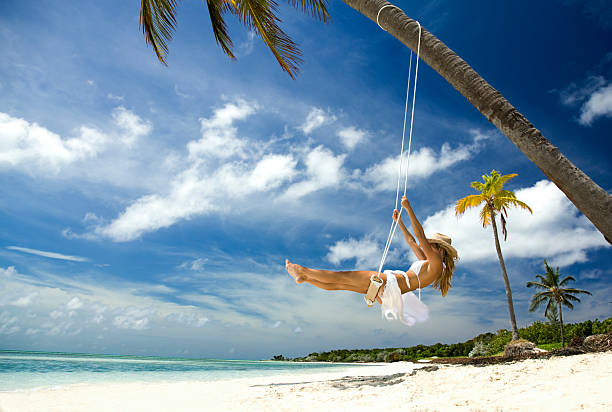 woman in cowboy hat swinging at a tropical beach stock photo
