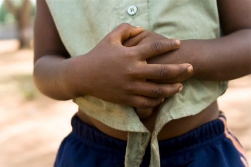 A little African girl with hands over her stomach symbolizing hunger.