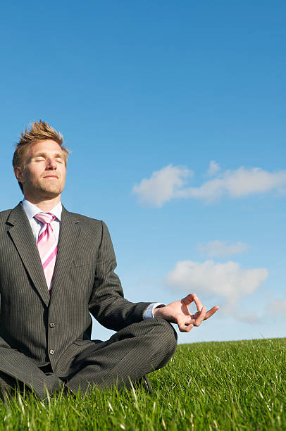 empresário fica ao ar livre meditating de pernas cruzadas no meadow - men yoga meditating cross legged - fotografias e filmes do acervo