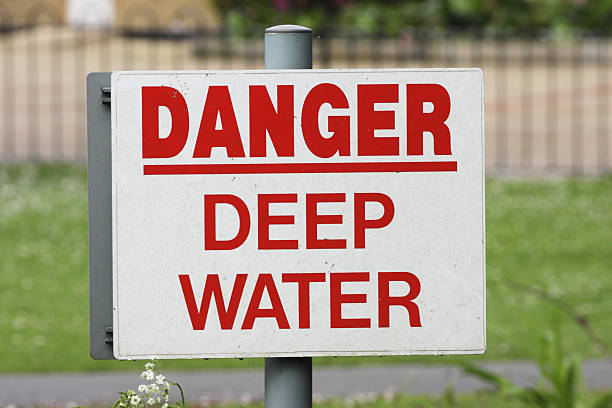 Red letter on white sign / notice on a quiet stretch of the River Wandle in Surrey, UK - Danger, Deep Water.