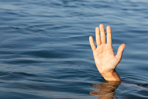 Hand of an unrecognizable person who is reaching for help and is drowning. Representing refugee deaths in the sea.