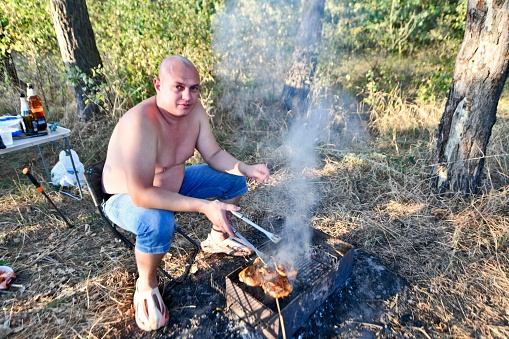 An adult man roasts meat in the forest in the fall.