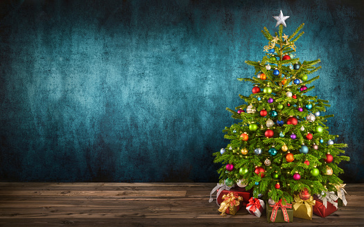 Delightful Christmas tree decorated with colorful ornaments placed on wooden floor, with teal textured wall as copy-space in the background