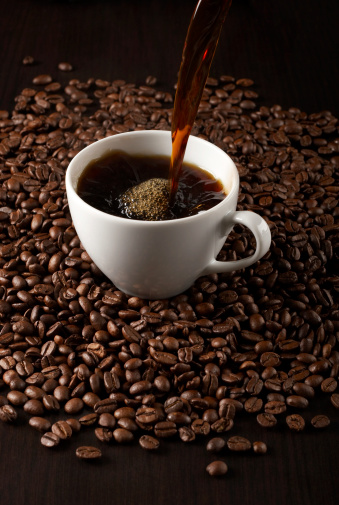 Pouring coffee into cup on background of coffee beans.