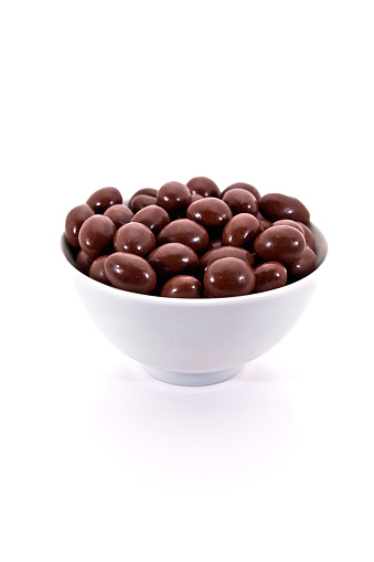 A bowl of chocolate covered almonds in white bowl.  Isolated on white.