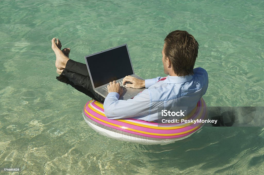 Uomo d'affari di galleggianti e funziona con anelli colorati mare tropicale - Foto stock royalty-free di Computer portatile