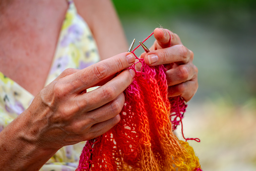 A woman knits a scarf with natural yarn