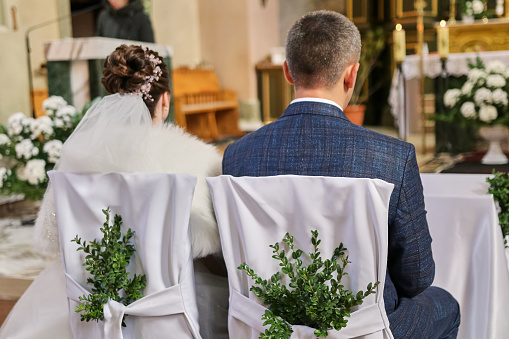 The bride and groom sit on chairs in the church during the wedding. Wedding ceremony.