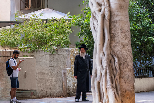 Tel Aviv, Israel - August 17, 2023: Hassidic older man looks at liberal young man, perhaps disapprovingly, in downtown Tel Aviv, Israel
