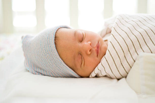 New-born baby sleeping on a bed wearing a blue hat stock photo