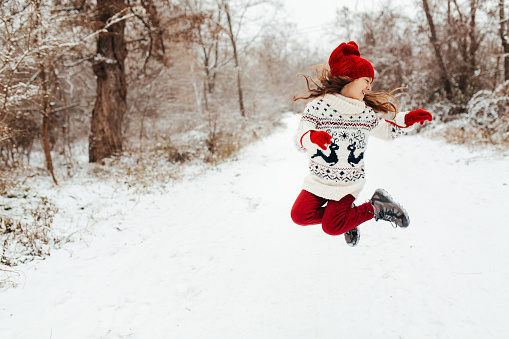 Playful little girl  jumping and enjoys playing on the snow in the forest