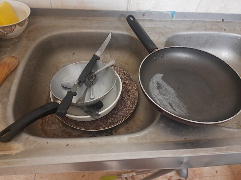 Dirty utensils, plates, bowls, spoons and knives in a metal sink