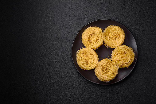 Raw capellini pasta or noodles with salt and spices on a dark concrete background