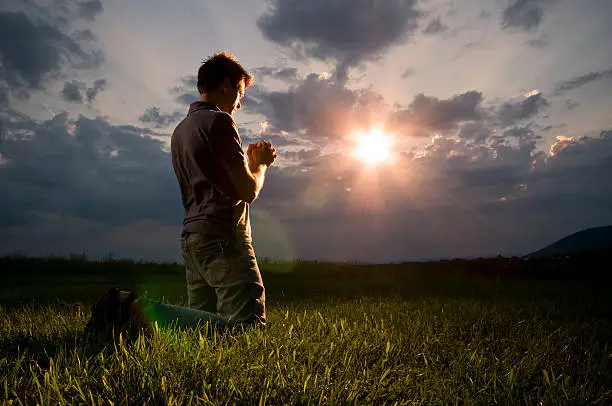 Young man on his knees praying with direct sun light into the camera.See also: