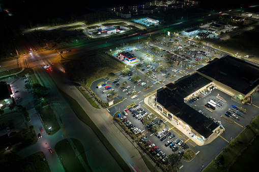 Aerial night view of many cars parked on parking lot with lines and markings for parking places and directions. Place for vehicles in front of a grocery mall store.