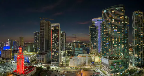 Photo of View from above of brightly illuminated skyscraper buildings in downtown district of Miami Brickell in Florida, USA at night. American megapolis with business financial district