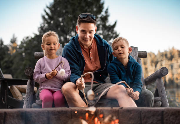 Father and children roasting marshmallows by a fire.
