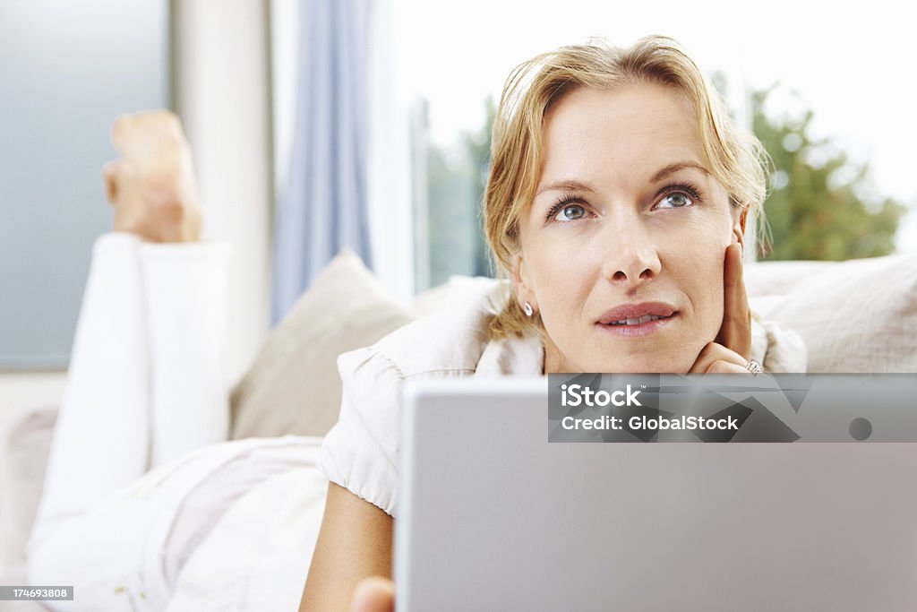 Mujer de mediana edad usando una computadora portátil y pensamiento - Foto de stock de Alerta libre de derechos