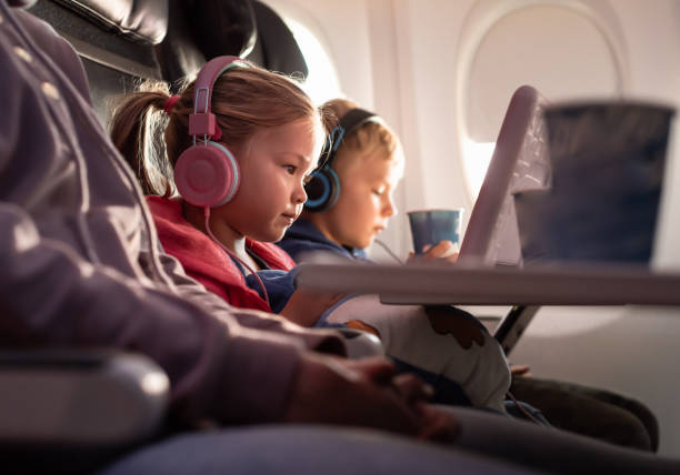 Menina e menino bonitos usando tablet digital enquanto voa em um avião. - foto de acervo