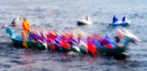 Rowing team in a dragon boat racing on a river, blurred motion, physical exertion in athletic cultural activity