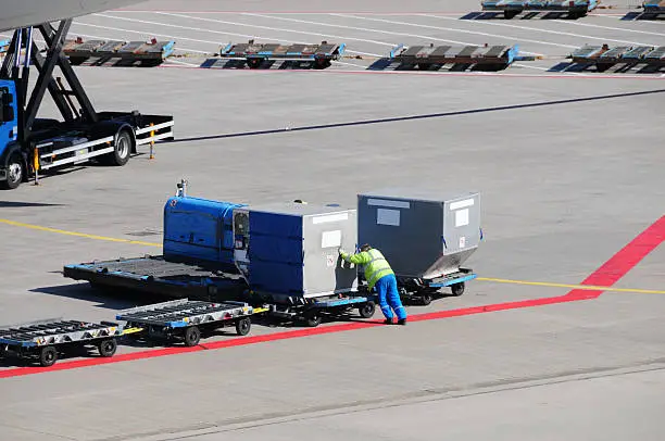 "Airport workers preparing cargo to be loaded on an airplane at Schiphol airport, the Netherlands."