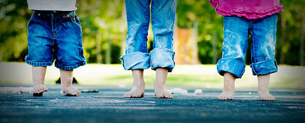tres hermanos de pie juntos. - child human foot barefoot jeans fotografías e imágenes de stock