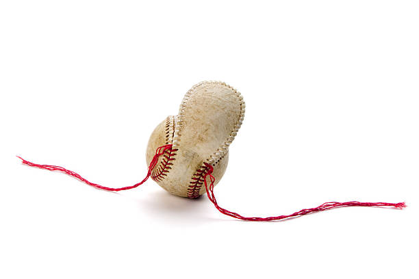 Old baseball with unstitched seams and loose cover "Old, worn baseball with red thread seams pulled out and loose leather cover flap. Overhead lighting, and red threads extending to sides of ball. Isolated on white." baseball threads stock pictures, royalty-free photos & images