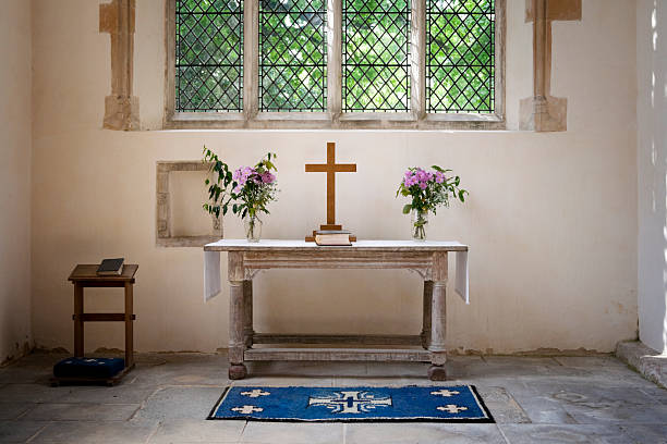 This photo captures the serene altar of Saint Thomas Church in Strasbourg, Alsace, France. The altar is adorned with symbolic elements, including a crucifix, an open Bible, and fresh flowers in a vase. Behind the altar, the high vaulted Gothic arches frame a modern cross installation, adding a contemporary touch to the historic setting. The stained glass windows and ornate chandeliers enhance the sacred atmosphere, reflecting the spiritual and architectural heritage of this iconic Protestant church.