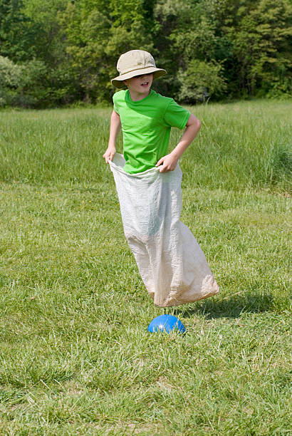 menino gunny corrida de saco, escola primária field day olhando para trás - child playing sack race sports race - fotografias e filmes do acervo