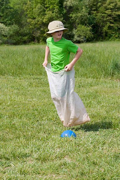 мальчик gunny бег в мешках, начальная школа поле день глядя на спине - child playing sack race sports race стоковые фото и изображения