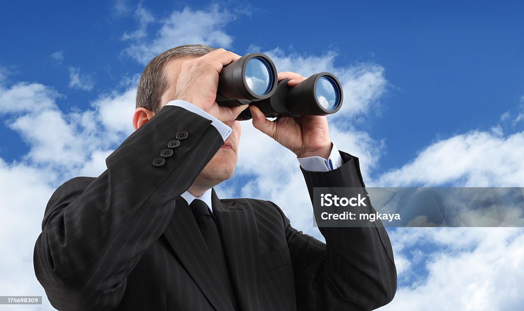 A businessman looking through binoculars Businessman looking through a binoculars with a reflection of a blue and cloudy sky. Binoculars Stock Photo