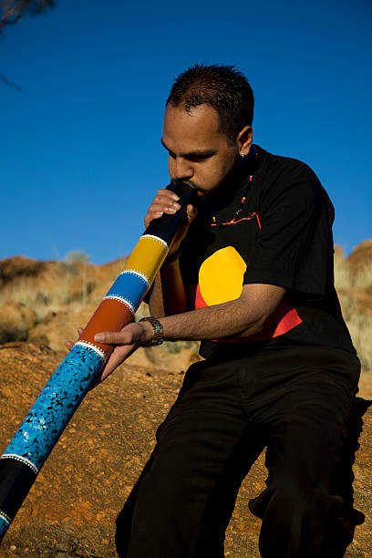 Aboriginal man playing a colorful didgeridoo A young Aboriginal man playing a colourful painted didgeridoo in the outback of Australia. didgeridoo stock pictures, royalty-free photos & images