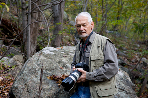 Retired senior man in forest with camera enjoying nature photography.