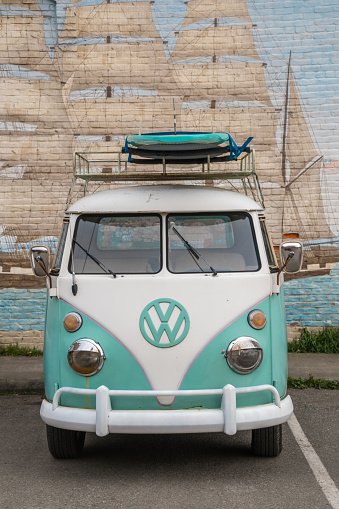 Port Townsend, WA, US-March 25, 2022:  Vintage 1960s blue-green VW kombi camper van or microbus modified as a pick-up with surfboards on roof parked on street.