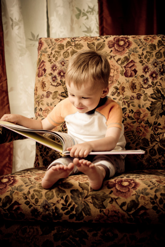 A small boy reads a large book alone