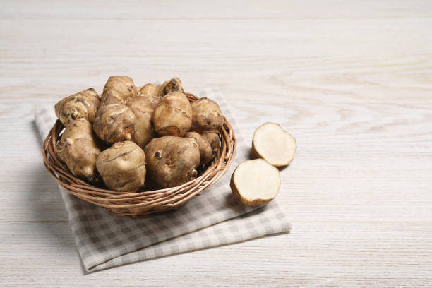 Wicker basket with many Jerusalem artichokes on white wooden table, space for text Wicker basket with many Jerusalem artichokes on white wooden table, space for text helianthus stock pictures, royalty-free photos & images