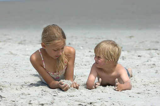 Sister and brother with Down Syndrome playing with sand at the beach.