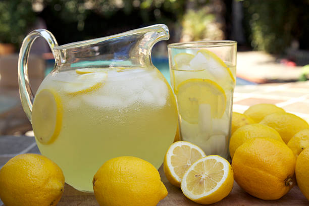 Round glass jug of fresh lemonade with sliced lemons at pool stock photo