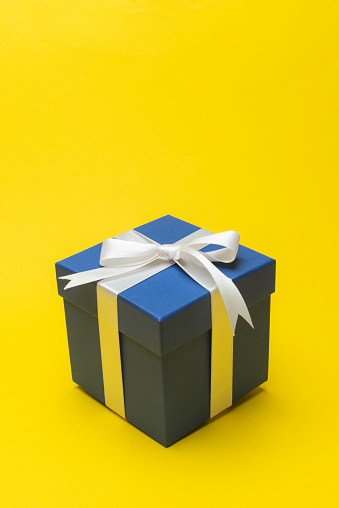 Blue giftbox with white ribbon on yellow background.