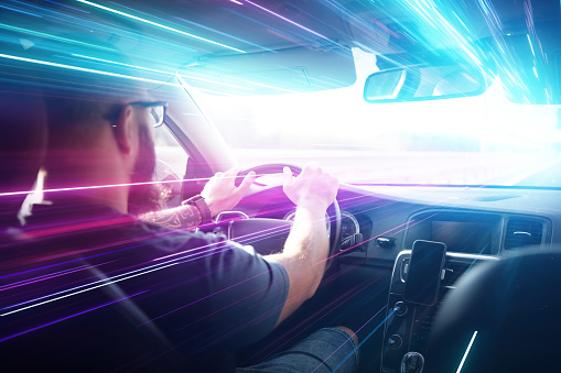 A man driving a car. Bright purple and cyan rays coming through the windshield, zoom in effect, hyper jump effect