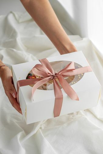 Young girl pastry chef holding a gift box with ribbons on a light background