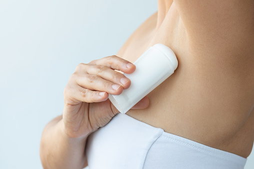 Midsection of an unrecognizable caucasian female is using antiperspirant in front of white background.