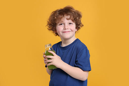 Cute little boy with glass bottle of fresh juice on orange background