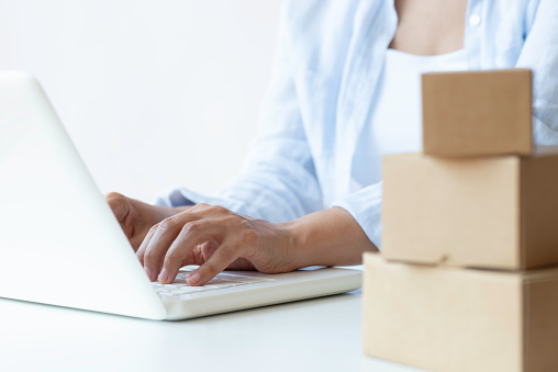 Unrecognizable female is using laptop  sitting among  delivery cartoon boxes. Representing online orders, e-commerce and home delivery.