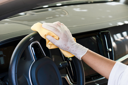 Unrecognizable female is cleaning steering wheel of her car.