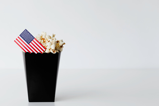 Black popcorn bag in front of white background with American flag. Representing film industry in America.
