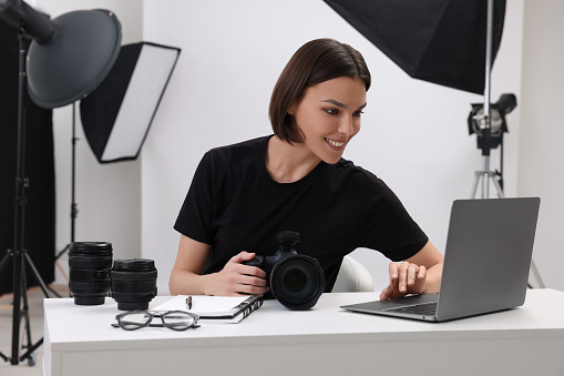 Young professional photographer with camera working on laptop in modern photo studio