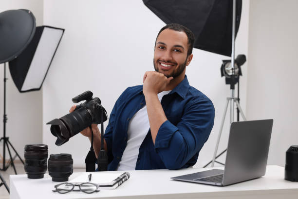 現代の写真スタジオのテーブルにカメラを持つ若いプロの写真家 - office tool flash ストックフォトと画像