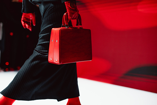 Fashion details of black long skirt, red gloves and leather handbag.