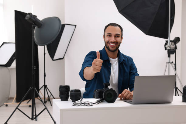 現代の写真スタジオで親指を立てるカメラを持つ若いプロの写真家 - office tool flash ストックフォトと画像